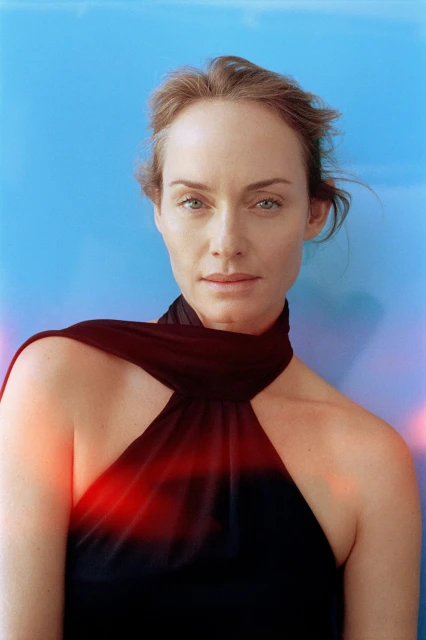 Portrait of a fair-skinned adult woman with shoulder-length hair against a graduated blue background, wearing a sleeveless black dress.