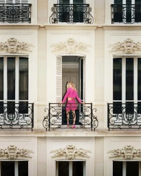 Gigi Hadid standing on a neoclassical balcony wearing a bright pink matching set for Self-Portrait Fall 2023 campaign.
