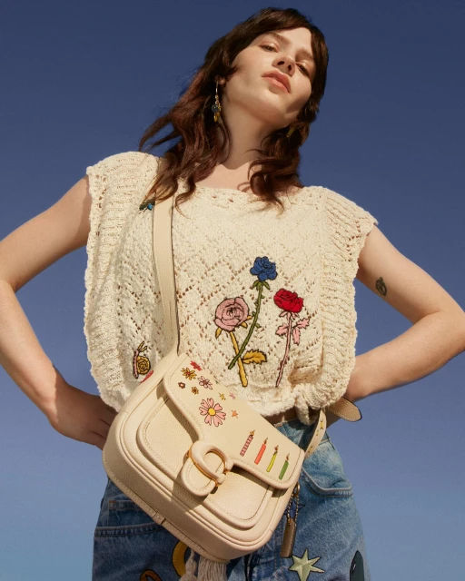 Fashion shot of a woman wearing a cream-colored crochet top and jeans, accessorized with a cream-colored purse and dangling earrings.