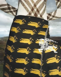 Close-up of a person wearing a duck-patterned black wrap skirt and check knit top against an overcast outdoor landscape.