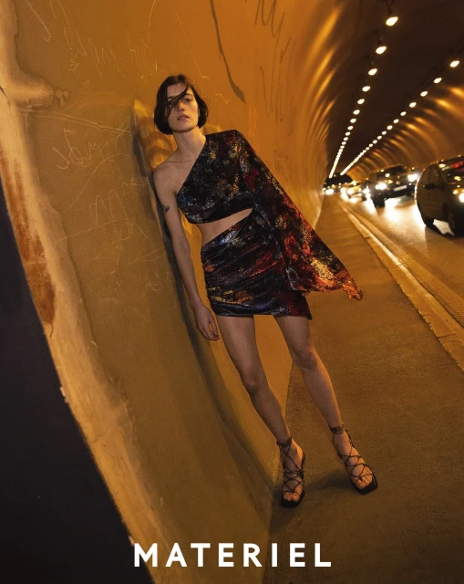 Fashion shot of a woman in a tunnel wearing a one-shoulder, multicolored, two-piece outfit with lace-up heeled sandals.