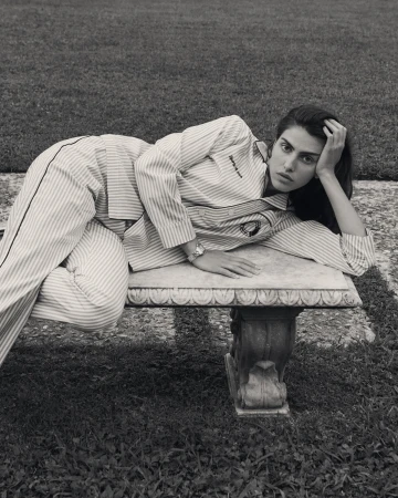 Monochrome portrait of woman in striped pajamas reclining on stone bench in outdoor garden setting, featuring wristwatch detail.