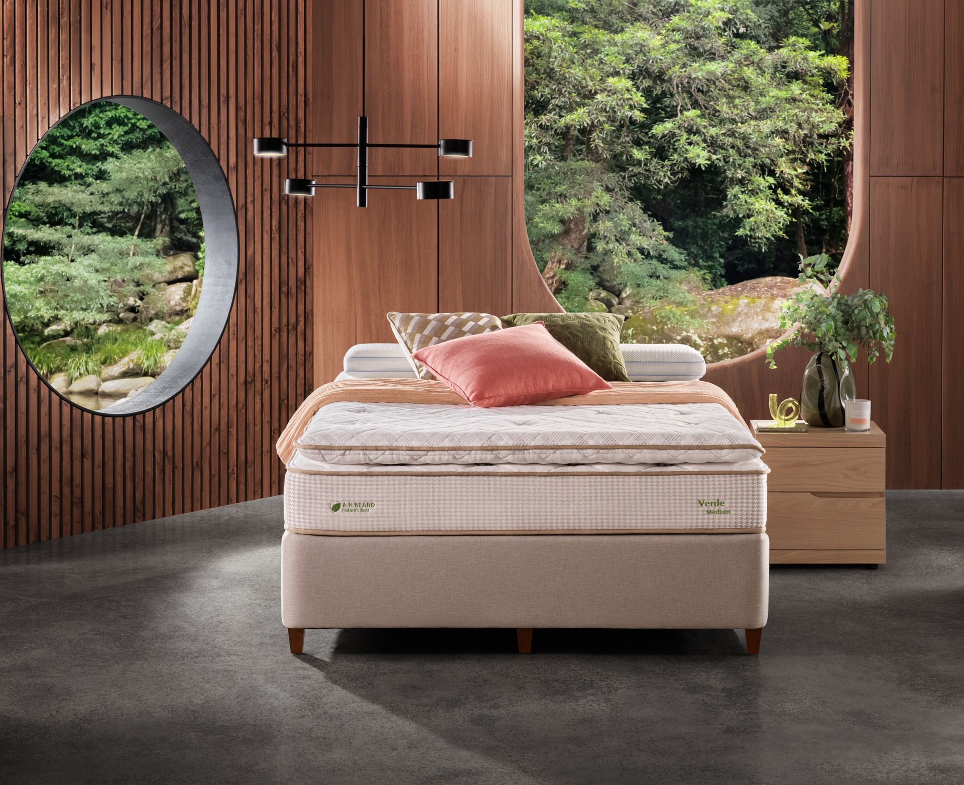 Bedroom setup featuring an inviting bed with decorative pillows, a wooden bedside table, and a view of lush greenery through a round window.