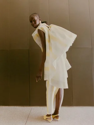 Model Ajok Madel wearing a striped white and yellow ensemble against a paneled wall for Harper's Bazaar España