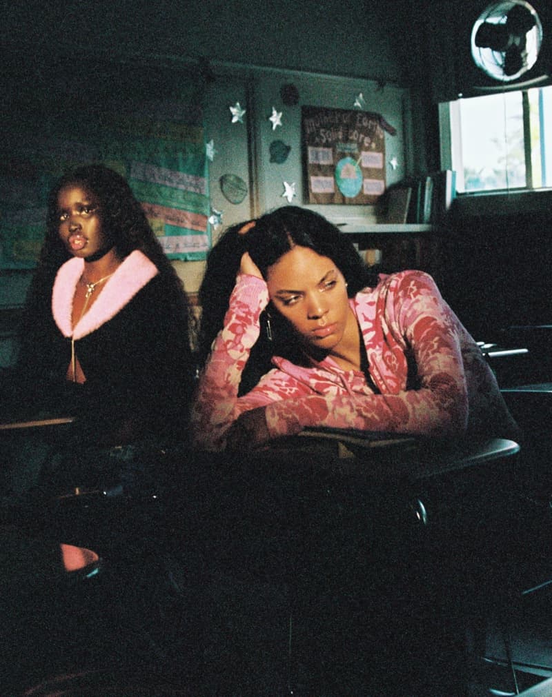 Two women in a classroom setting. One woman wears a pink floral top with her head in her hand and the other is wearing black