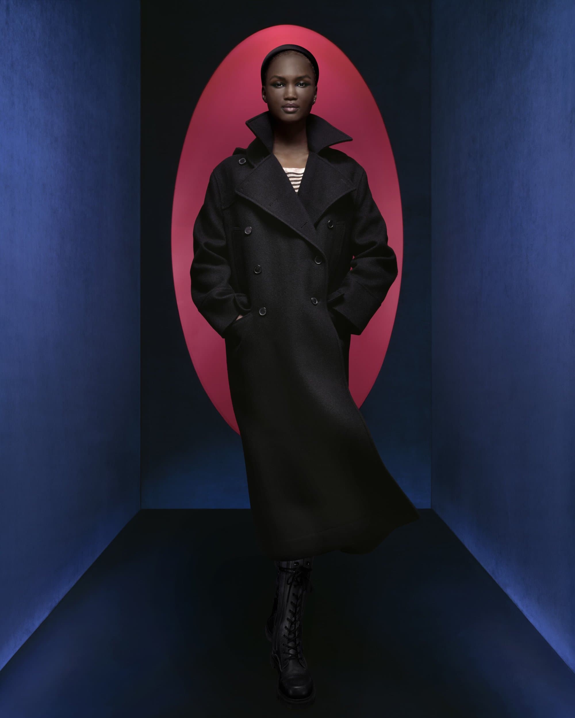 Elegant Black Woman in Long Coat: Posing indoors with red and blue illuminated background. Fashion, sophistication, and style combined.