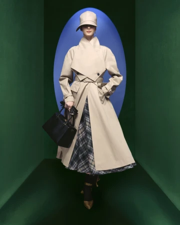Model wearing a beige structured trench coat, matching cloche hat, and holding a black handbag in a green frame with a blue oval.