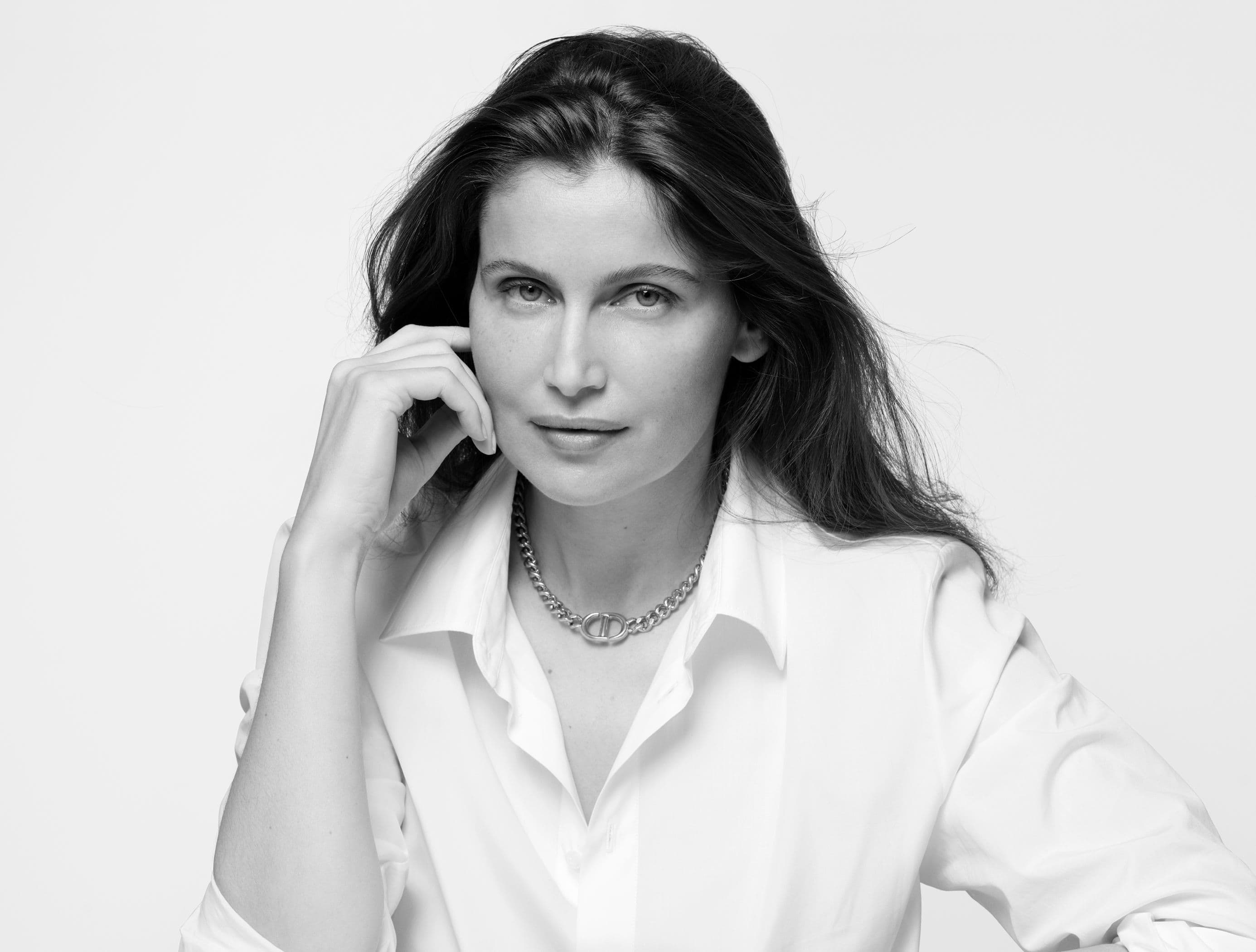 Black and white portrait of a woman with dark hair wearing a chain necklace and a white blouse against a bright background.