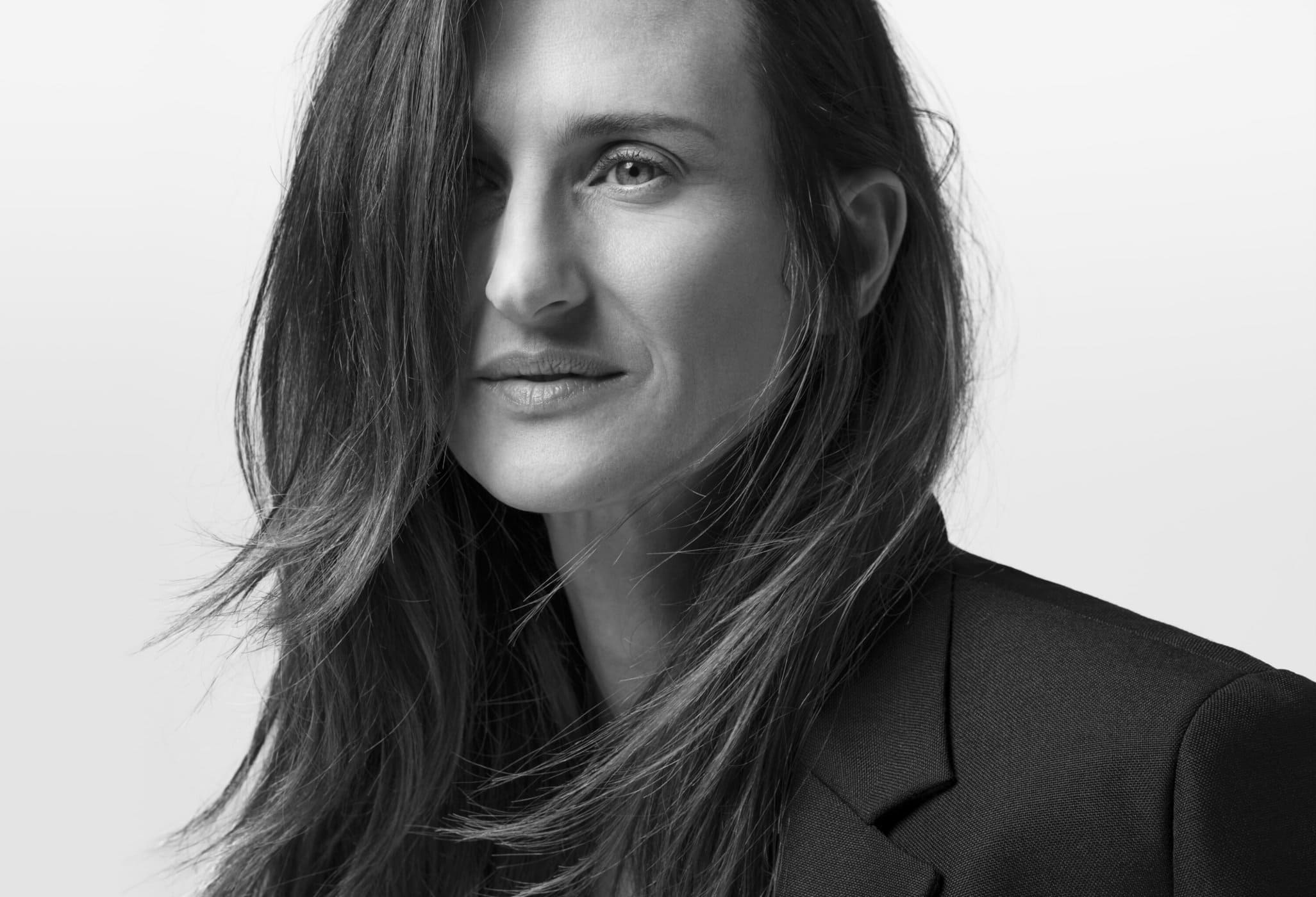 Black and white portrait of an adult woman with long hair, wearing a blazer, against a neutral background, photographed in a photo studio.