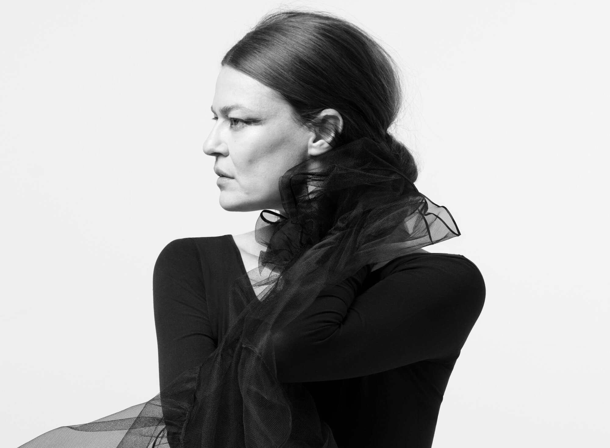 Black and white portrait of an adult woman looking to the side, with long brown hair, wearing a black top and tulle collar.