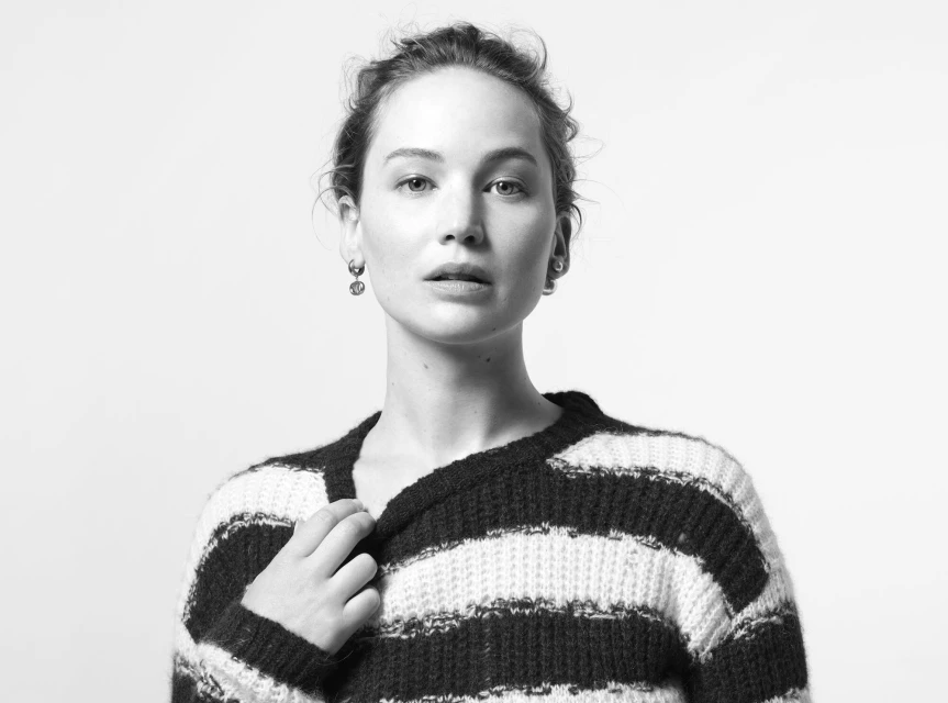 Monochrome portrait of a woman with fair skin and wavy hair wearing a striped sweater, looking directly at the camera in a studio.