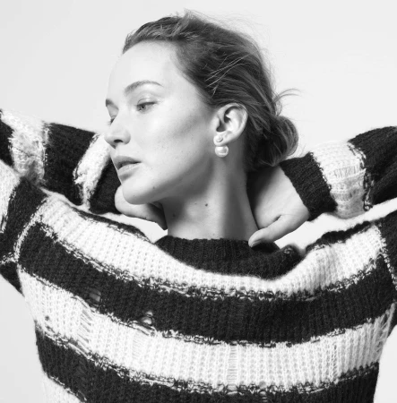 Monochrome portrait of a woman in a striped sweater with a neutral expression, gazing slightly down with hands behind her head.