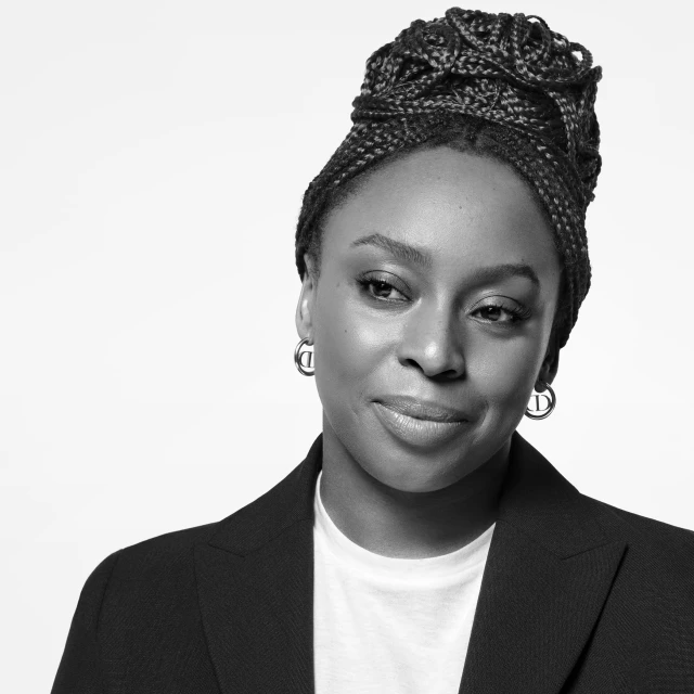 Black and white close-up portrait of a woman with braided hair, wearing a dark blazer over a white t-shirt against a white background.