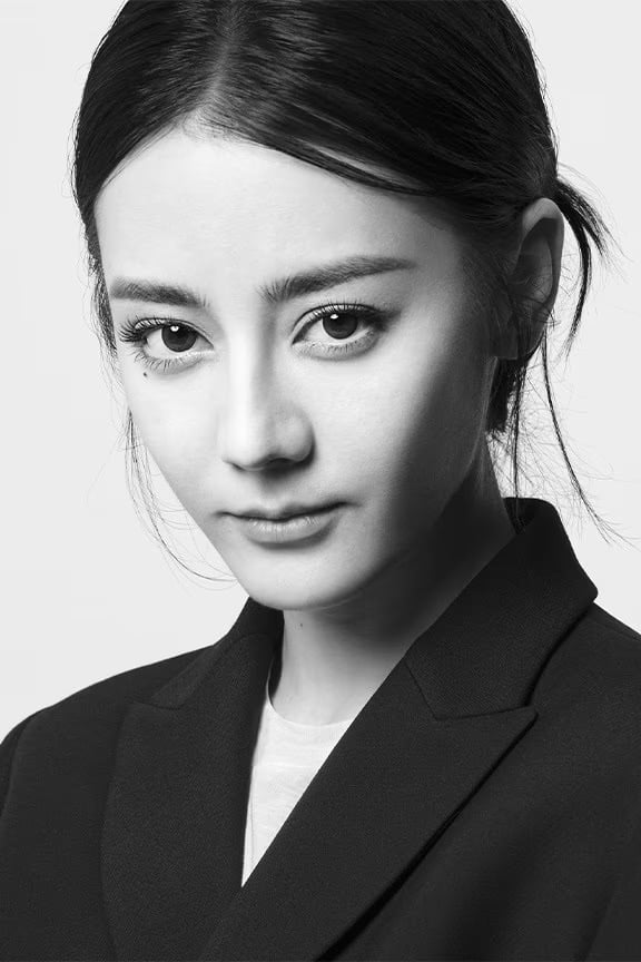 Portrait of a woman in a black blazer with dark hair pulled back, posing against a white background in a close-up shot.
