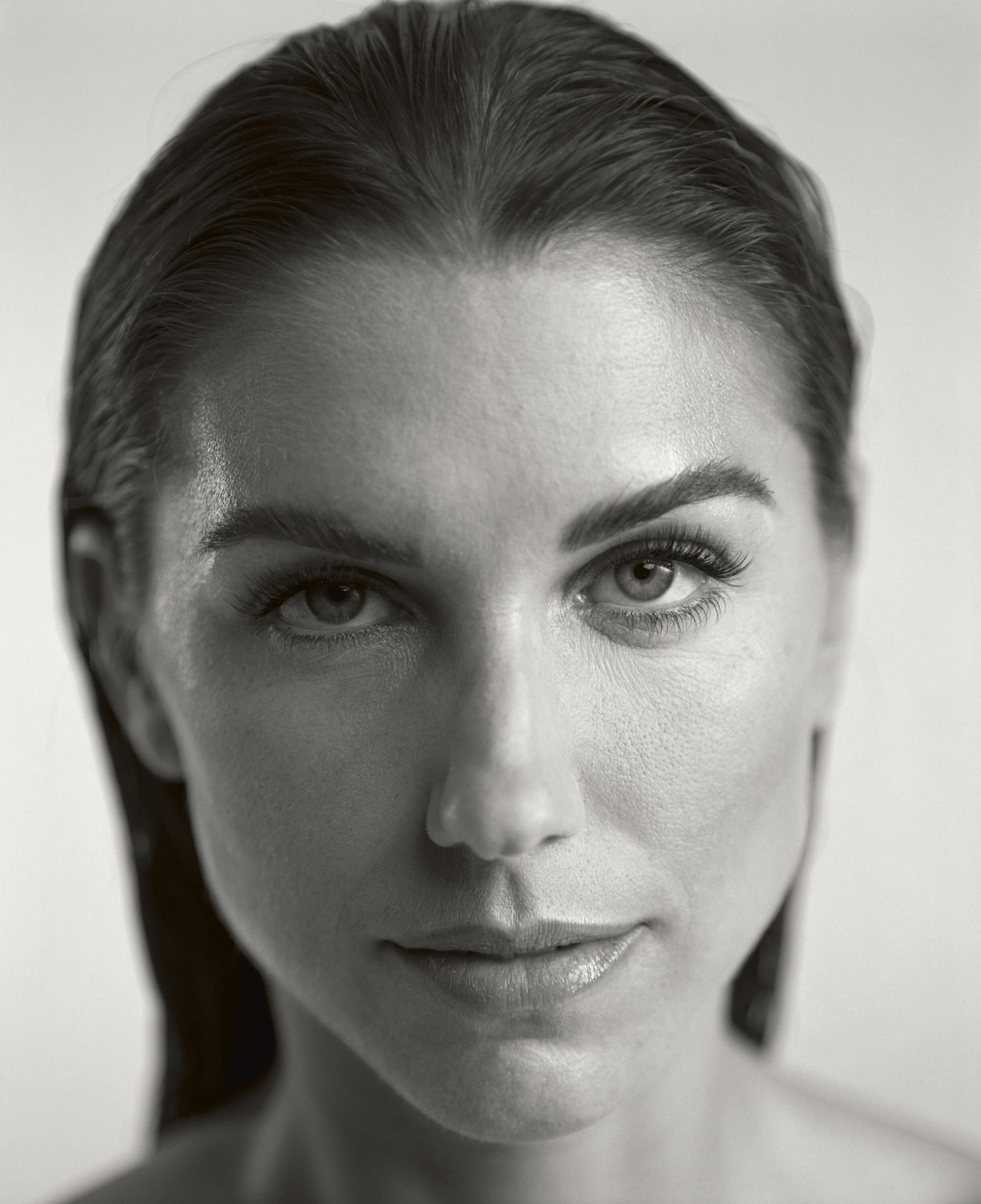 Close-up portrait of a woman with slicked-back hair, focusing on her facial features in a black-and-white studio setting.