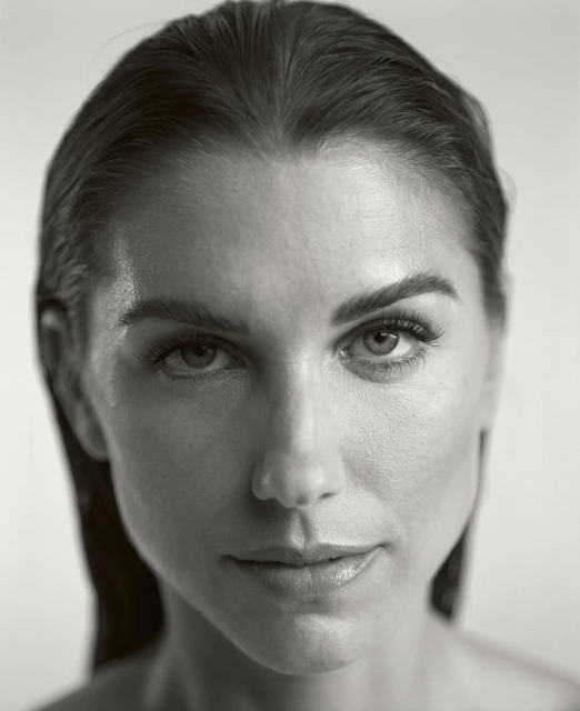 Close-up portrait of a woman with slicked-back hair, focusing on her facial features in a black-and-white studio setting.