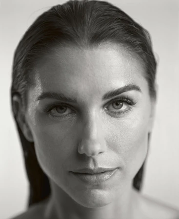 Close-up portrait of a woman with slicked-back hair, focusing on her facial features in a black-and-white studio setting.