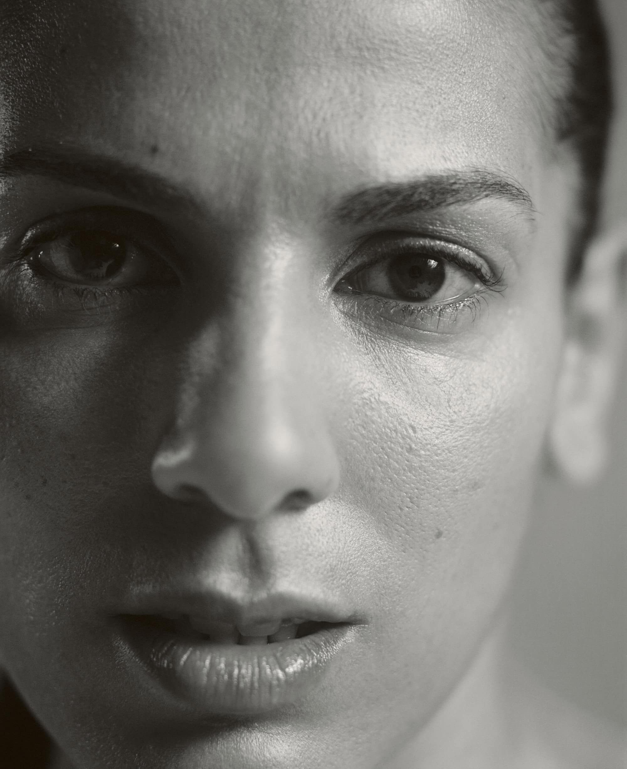 Striking black and white portrait of an adult woman, captured in a close-up shot that highlights her facial details and intense gaze.
