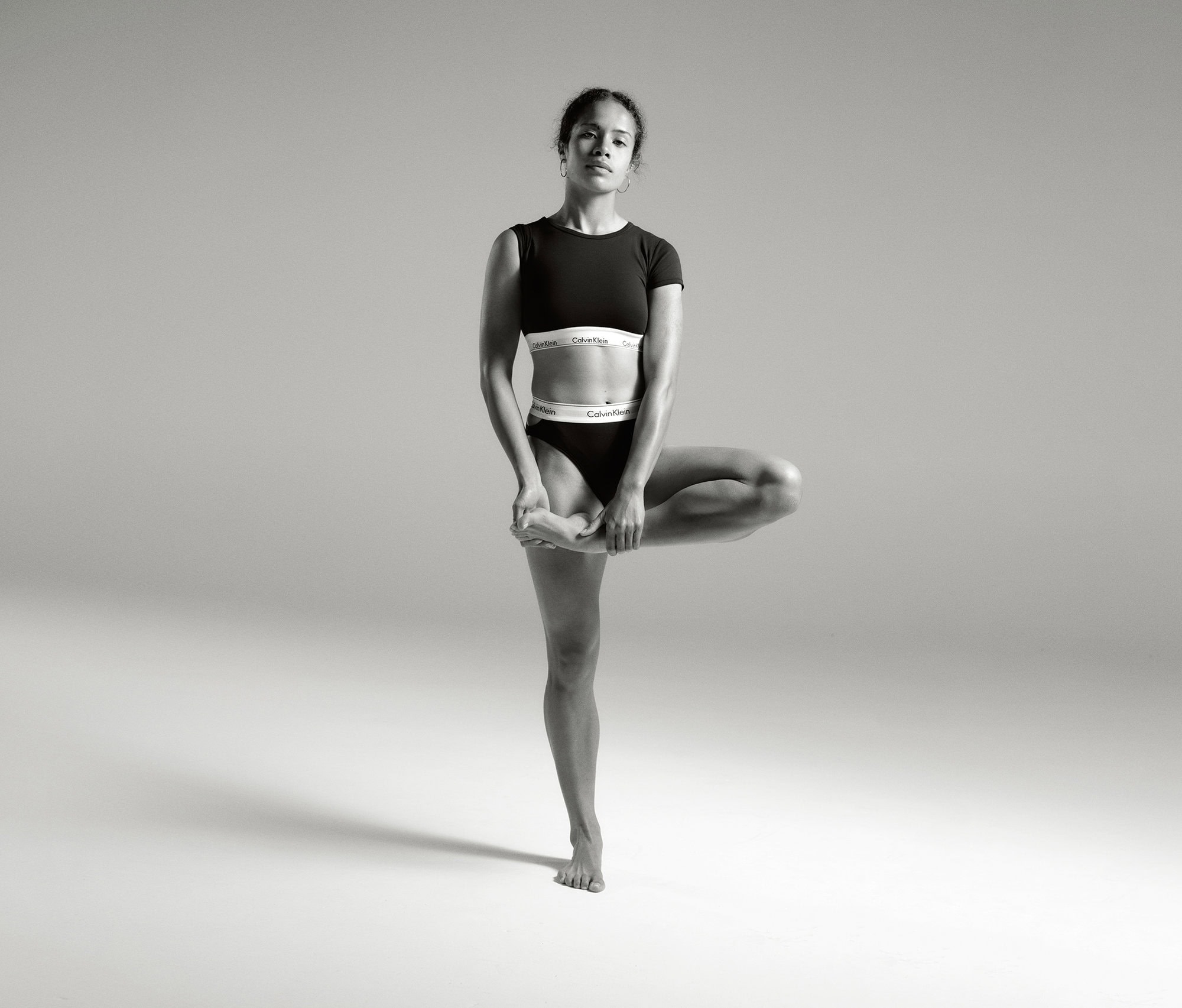 A woman in athletic wear balances in a tree pose against a neutral backdrop, highlighting fitness and minimalist sportswear fashion.