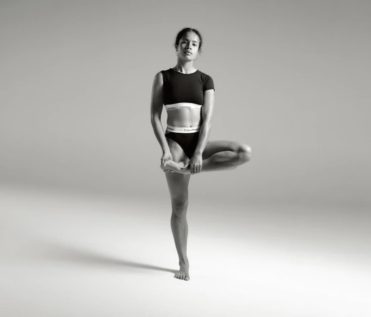A woman in athletic wear balances in a tree pose against a neutral backdrop, highlighting fitness and minimalist sportswear fashion.