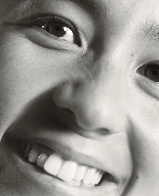 Close-up black and white portrait of a smiling woman. A high-angle captures her face, highlighting her eyes, nose, mouth, and teeth.