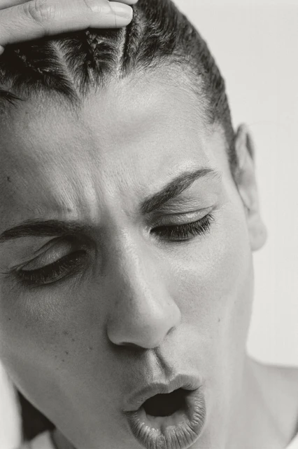 Monochrome close-up of an adult woman with braided hair touching her forehead, her eyes closed and her mouth open.