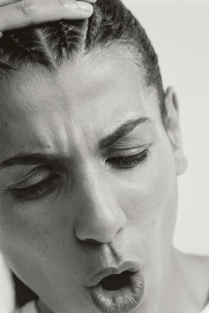 Monochrome close-up of an adult woman with braided hair touching her forehead, her eyes closed and her mouth open.