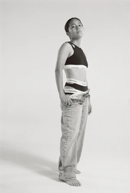 Monochromatic studio shot of a woman in Calvin Klein underwear and jeans, striking a confident pose against a bright backdrop.