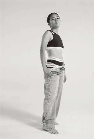 Monochromatic studio shot of a woman in Calvin Klein underwear and jeans, striking a confident pose against a bright backdrop.