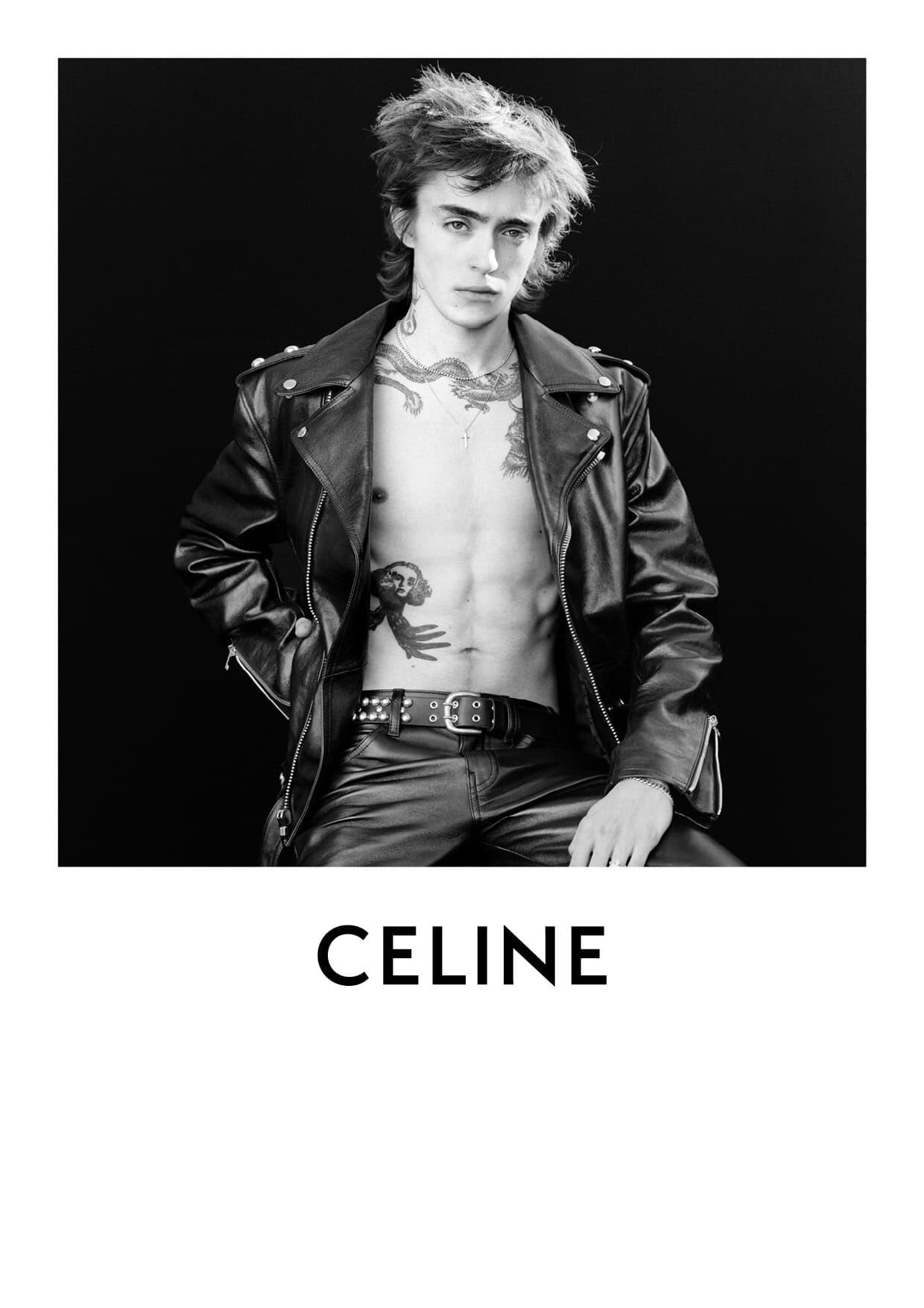 A monochromatic fashion portrait of a young adult male in a leather jacket and pants against a dark background, with the CELINE logo.