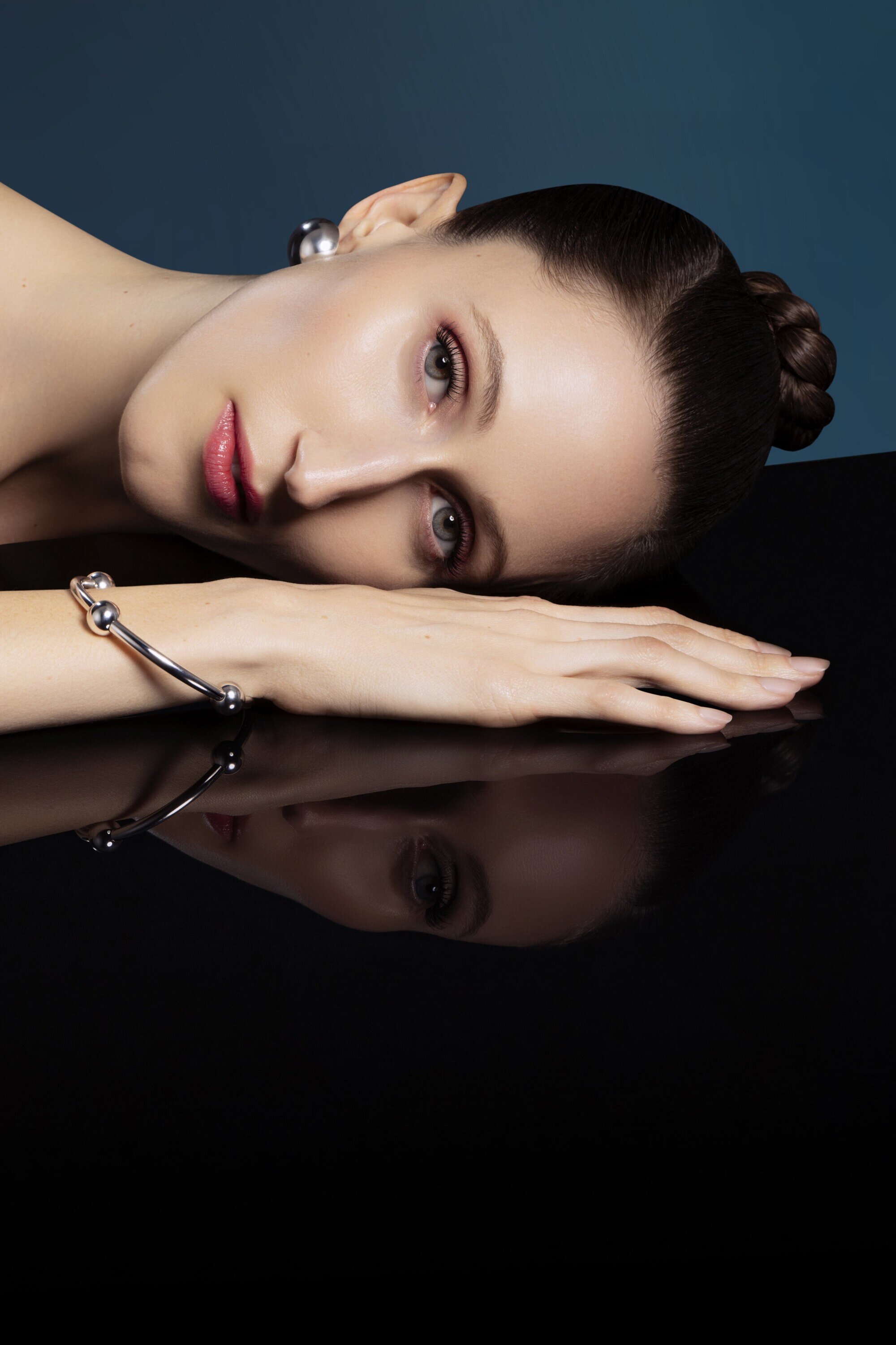 Close-up portrait of a woman with elegant updo and silver jewelry against a gradient blue backdrop, showcasing beauty and fashion.