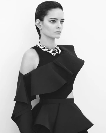 Model in black sculptural dress with chunky silver chain necklace against white background
