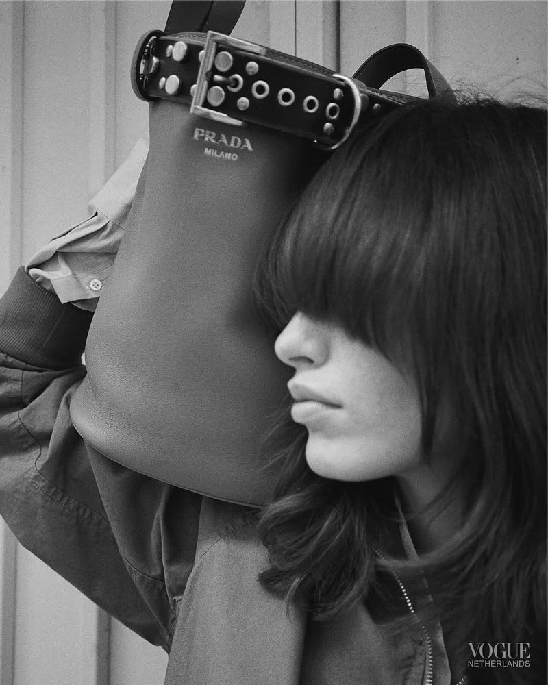 Monochrome fashion shot featuring a woman with bangs and Prada bag with a chunky studded strap, Vogue Netherlands logo visible.