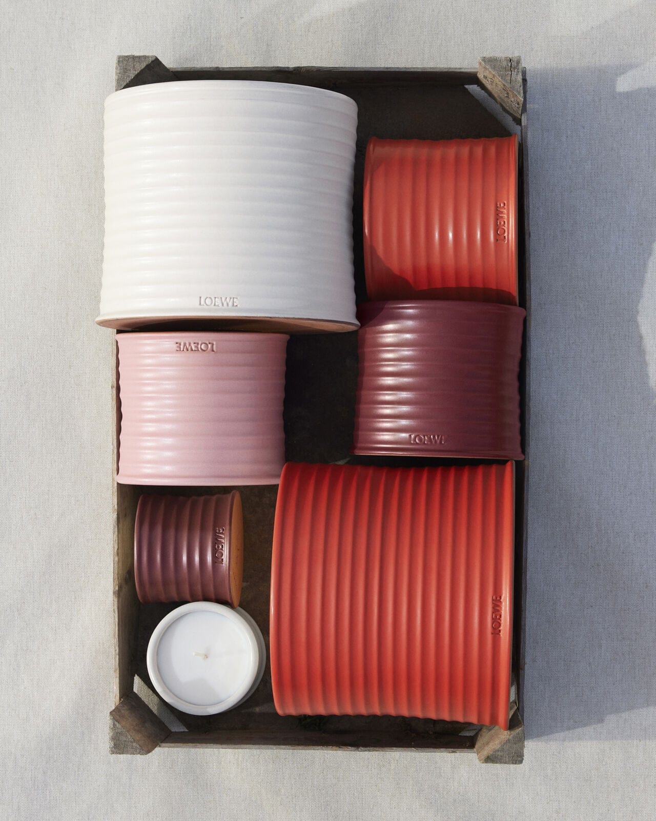 Cylindrical candles in various colors and sizes arranged neatly in a rustic wooden crate; minimalist aesthetic; product photography.
