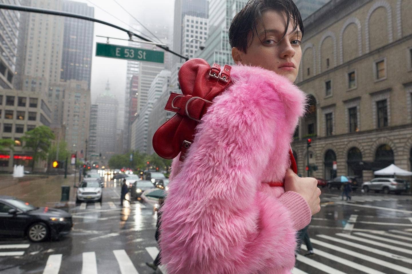 Fashionable person with pink fur coat in urban street scene. Cityscape backdrop with cars and 'E 53 St' sign.