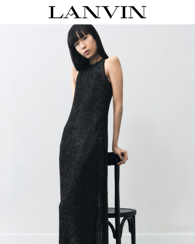 Elegant Asian woman in shimmering black halter gown leans on chair in studio for Lanvin fashion campaign against white backdrop.
