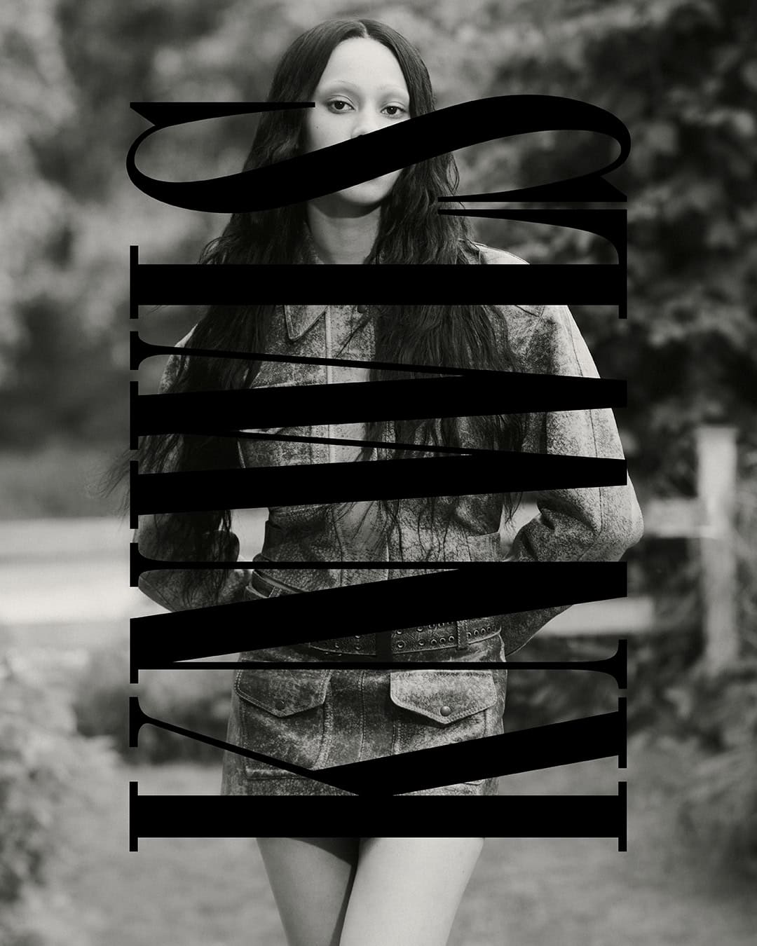 Black and white portrait of a person with long dark hair wearing a matching denim set, partially obscured by large black typography overlay.