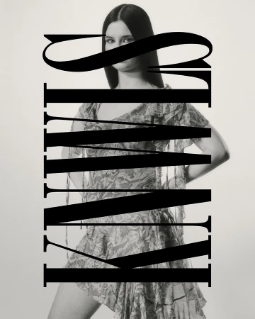 Monochromatic fashion shot of a slender adult woman wearing a floral mini dress, large typography overlay in studio setting.