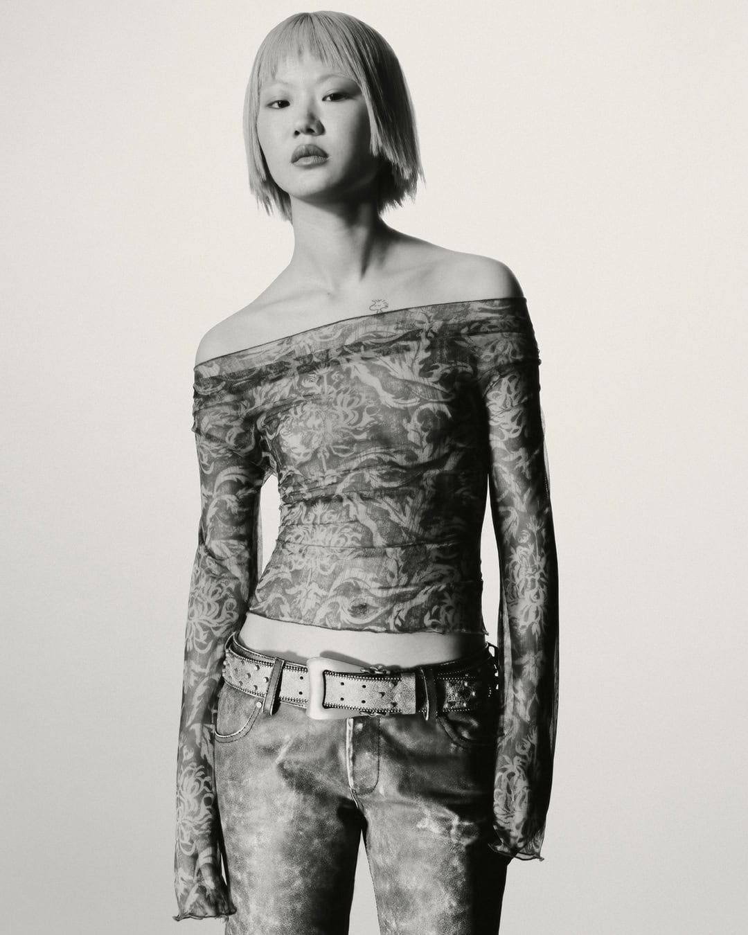 Model in printed sheer off-shoulder top and studded belt against a plain white background for KNWLS Proxy 2.0 campaign