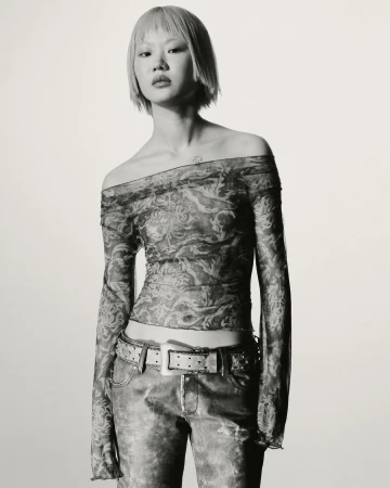Model in printed sheer off-shoulder top and studded belt against a plain white background for KNWLS Proxy 2.0 campaign