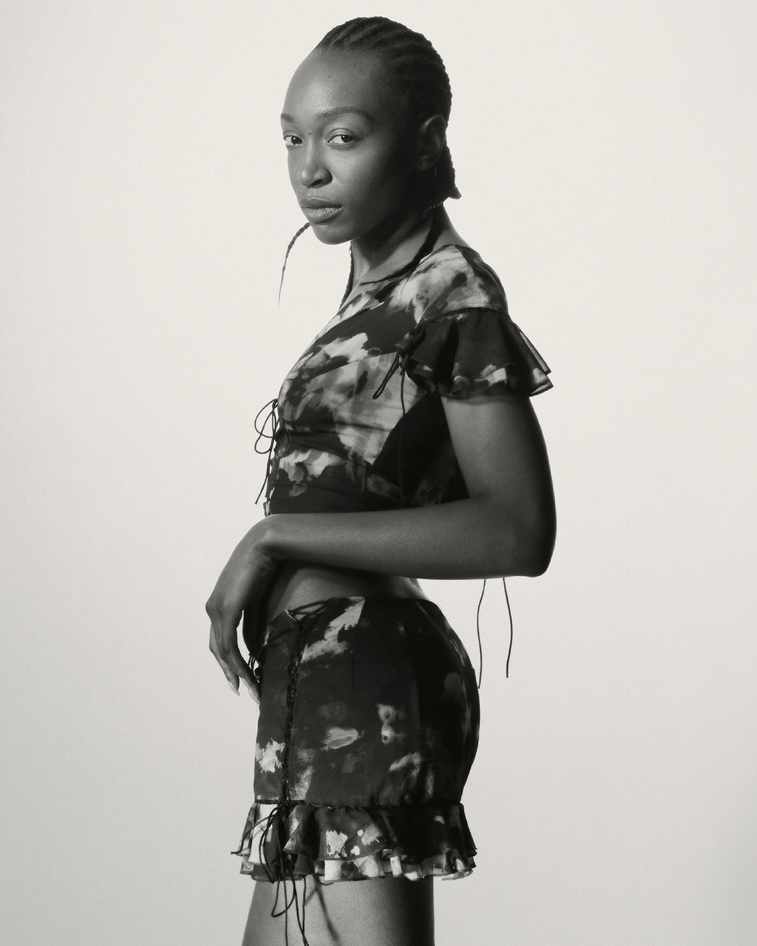 A slender woman in a patterned two-piece outfit poses against a plain backdrop, showcasing fashion and style in a studio setting.