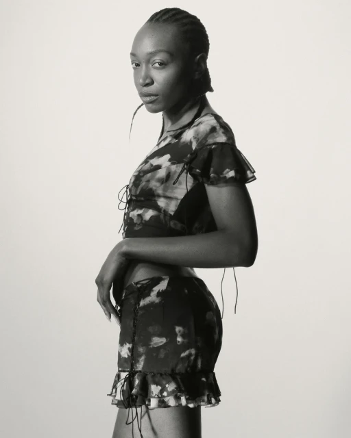A slender woman in a patterned two-piece outfit poses against a plain backdrop, showcasing fashion and style in a studio setting.