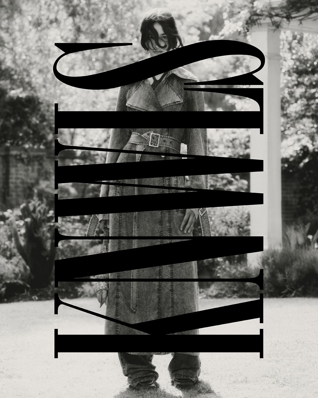 Monochrome portrait of a woman in a denim trench coat posing outdoors with bold typography overlaying the image, editorial fashion.