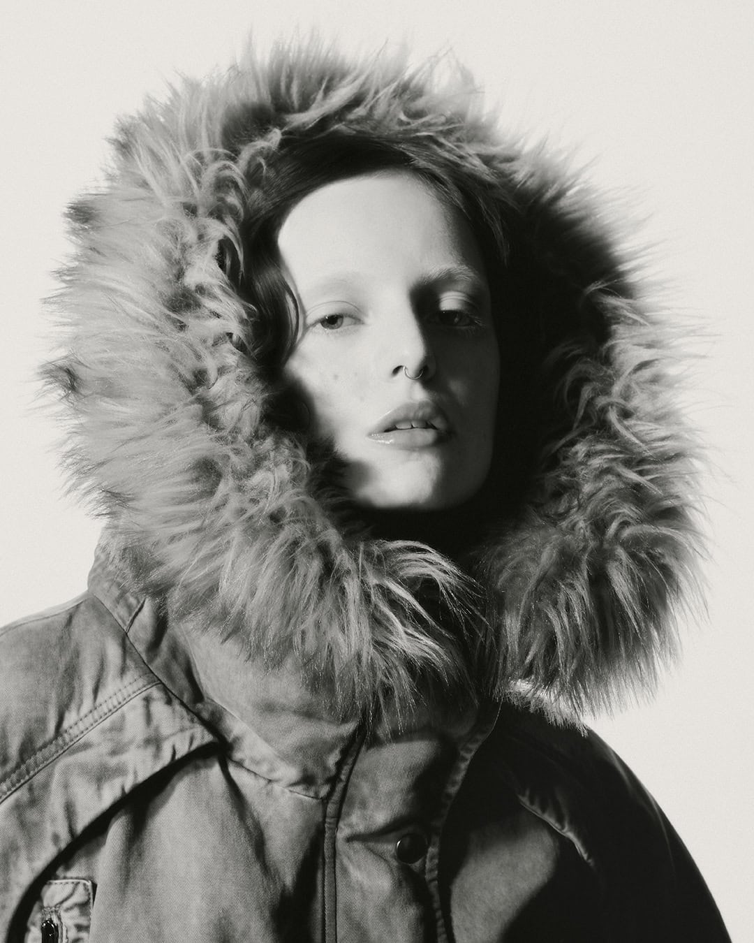 Portrait of a woman wearing a heavy winter jacket with a large fur-lined hood against a plain background.