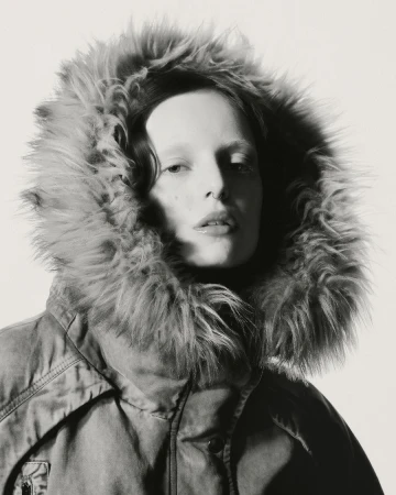 Portrait of a woman wearing a heavy winter jacket with a large fur-lined hood against a plain background.