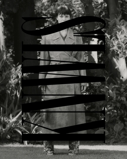 Monochrome portrait of a woman in a trench coat standing outdoors amongst lush foliage, partially obscured by large black typography.