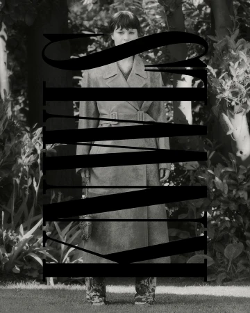 Monochrome portrait of a woman in a trench coat standing outdoors amongst lush foliage, partially obscured by large black typography.