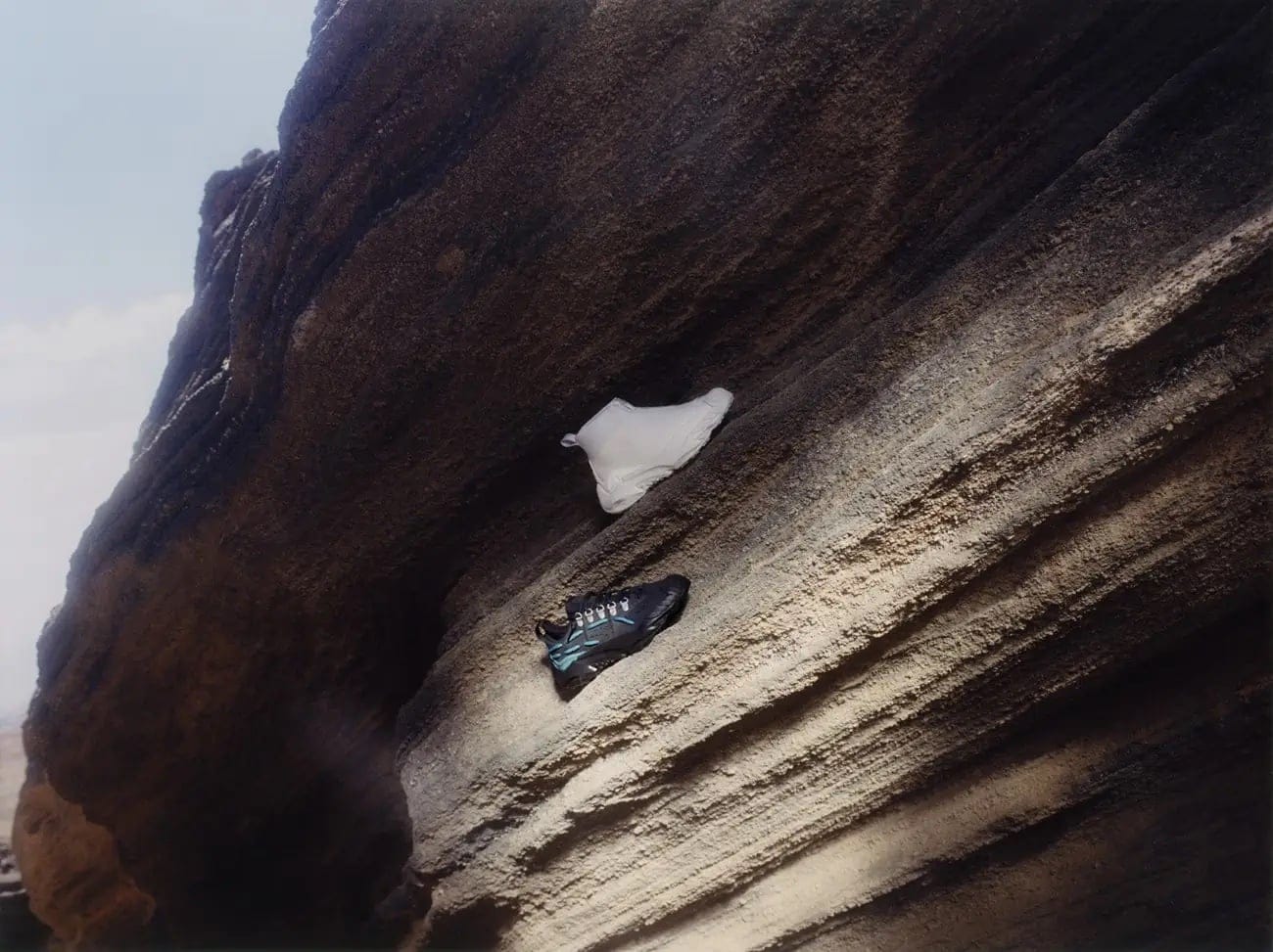 A closeup captures two shoes—a white slipper and a black running shoe—resting on a striated rock surface under natural lighting.
