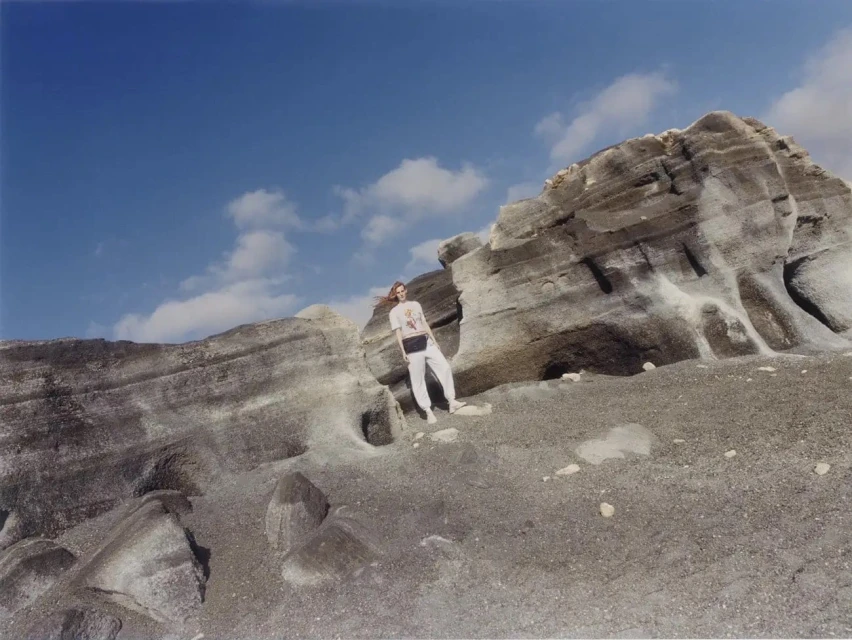 Adult female in casual clothing standing on a gray and white rocky hill under a partly cloudy sky in a full shot.