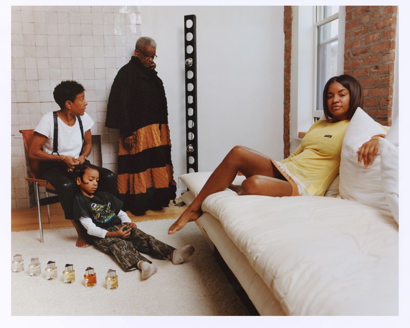 A family portrait in an interior setting features an adult female reclining on a couch and a child sitting near a collection of objects.